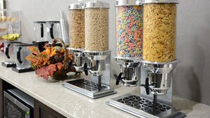Una estación de cereales autoservicio con diversas opciones, como copos de maíz, un tazón de fruta y una decoración otoñal.