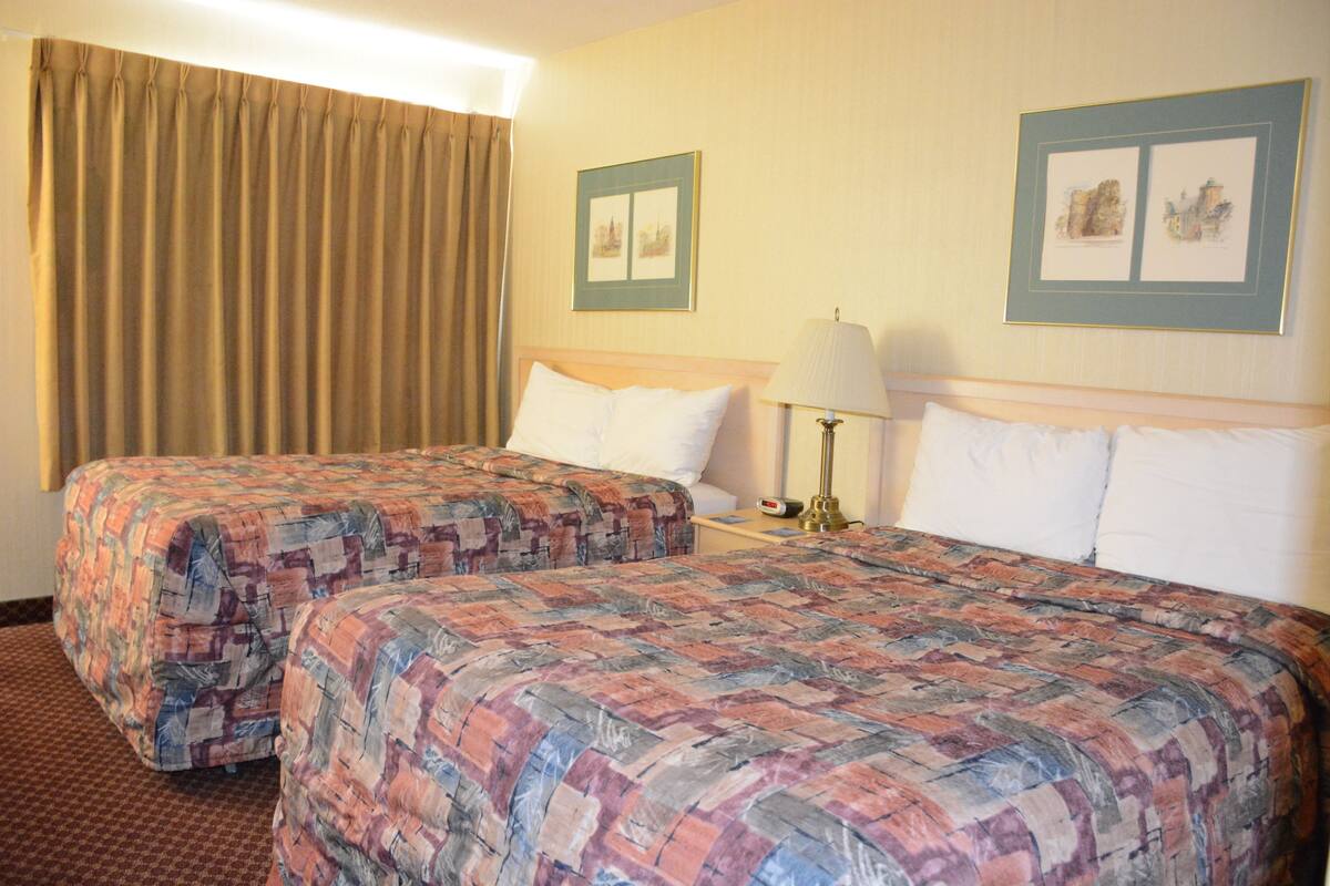 A hotel room with two beds, a nightstand with a lamp, and two framed pictures on the wall.