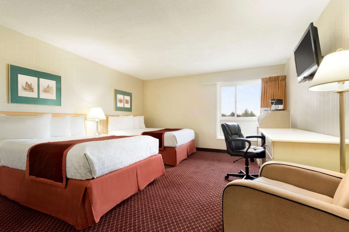 A hotel room with two beds, a desk, a chair, a TV, and artwork on the walls.