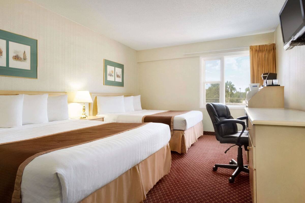 A hotel room with two beds, a desk, a chair, a TV, and a window.
