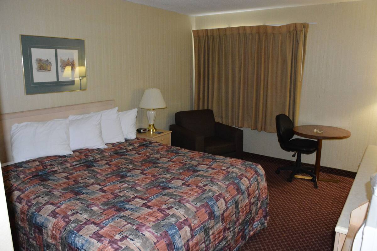 A hotel room with a large bed, a desk, a chair, and a lamp.