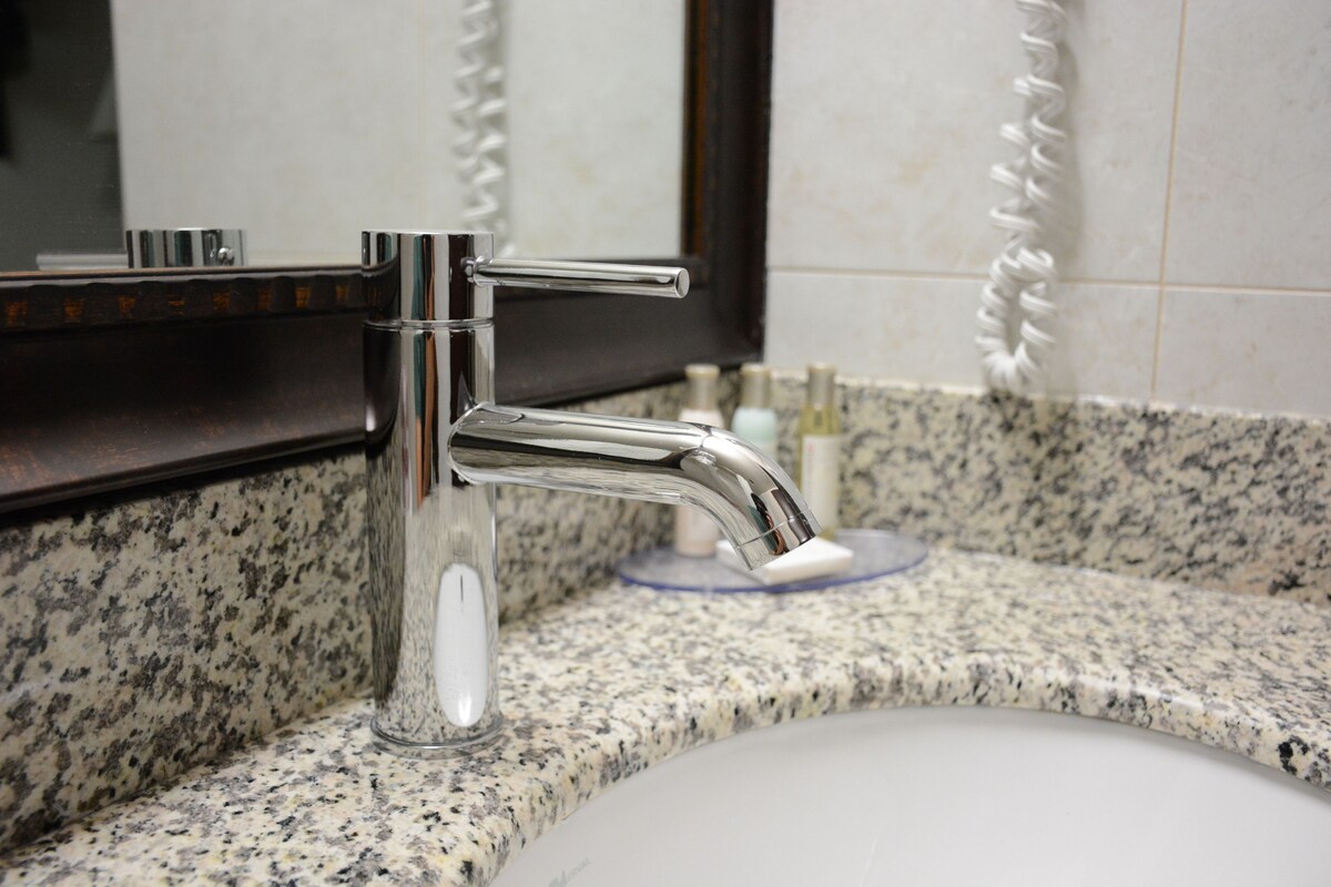 A bathroom sink with a chrome faucet, a mirror, and a granite countertop.