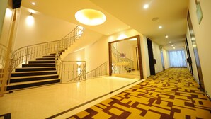 Un pasillo de hotel con alfombra estampada, una escalera con barandillas de metal y una lámpara en el techo.