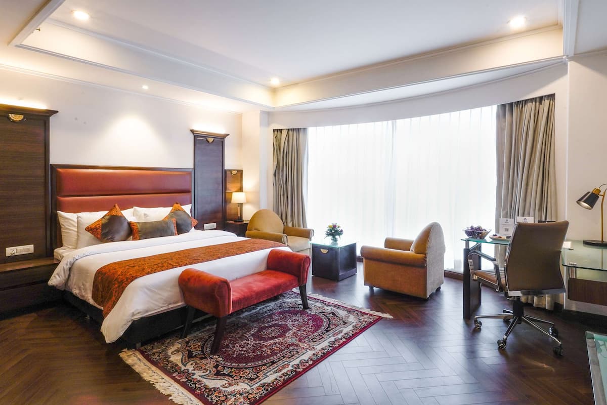 A hotel room with a large bed, a desk, a chair, and a small table.