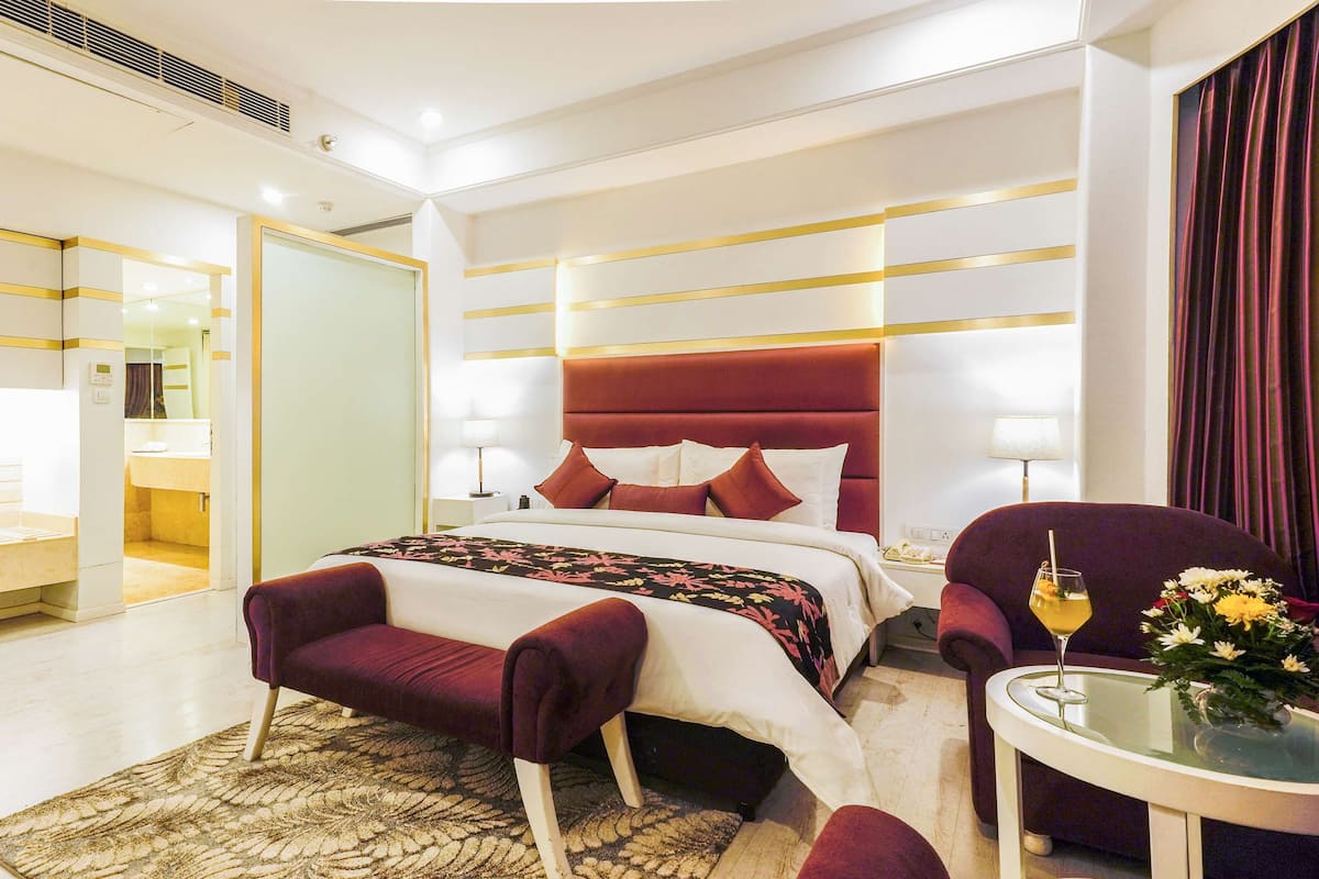 A modern hotel room with a large bed, a sitting area with a chair and a small table, and a bathroom visible through an open door.