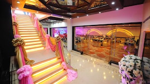 Una escalera con decoraciones rosa y dorado, un espejo que refleja un salón de banquetes y un candelabro.