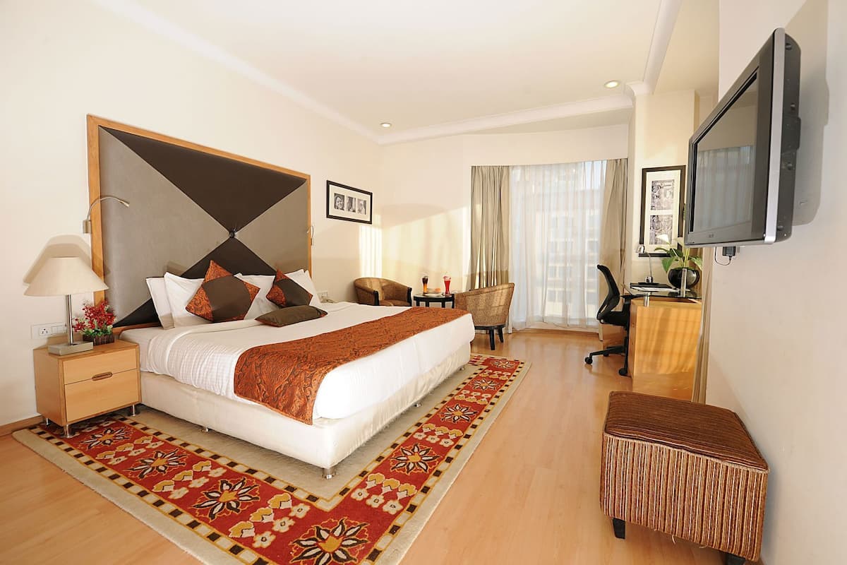A hotel room with a large bed, a desk, a chair, a TV, and a window with curtains.