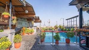 Un área de piscina en la azotea con plantas en macetas, una terraza de madera y vistas al horizonte de la ciudad.