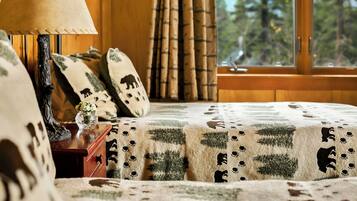 Un dormitorio con una cama cubierta por una colcha estampada, una mesita de noche con una lámpara y una ventana que ofrece vistas a árboles.