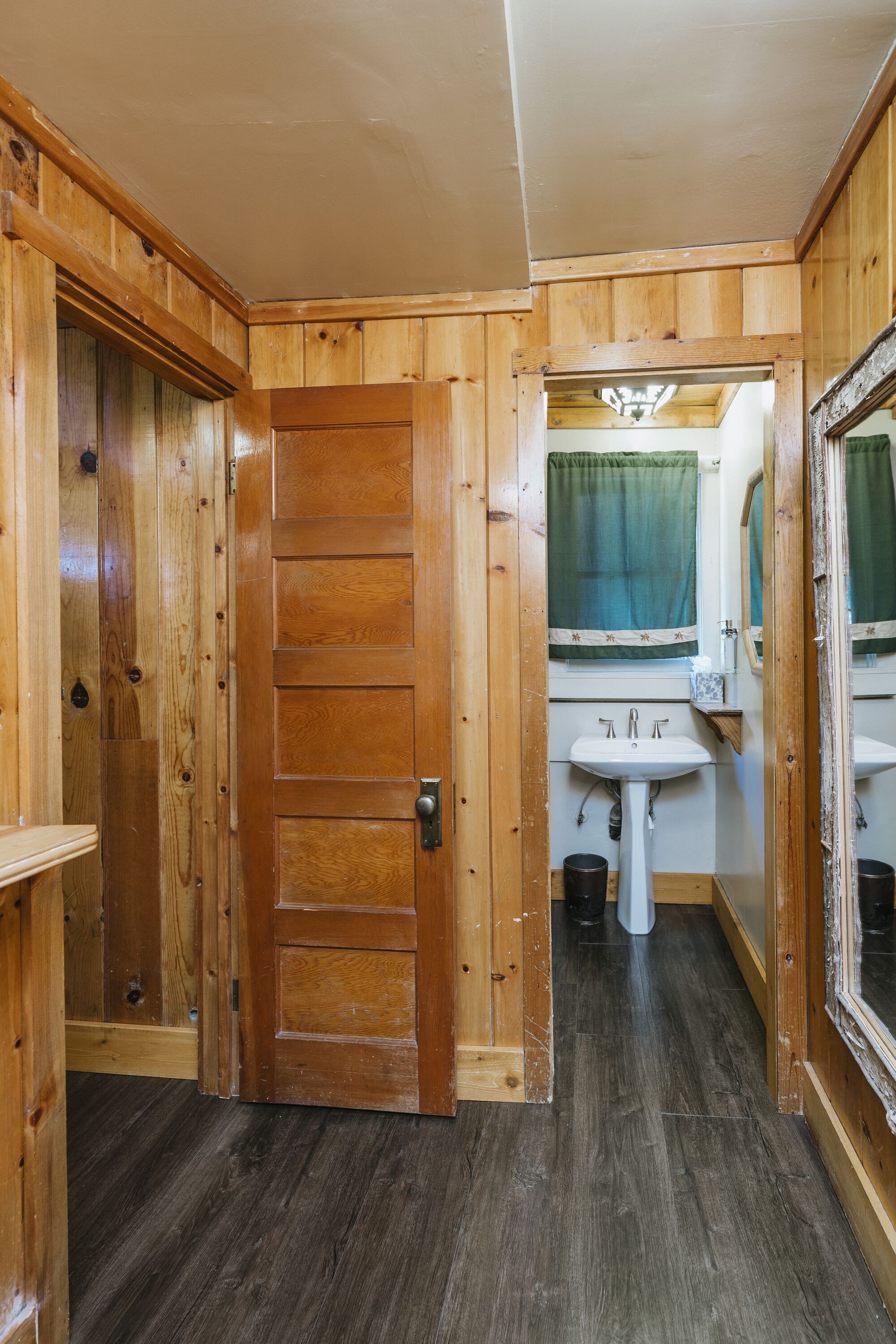 Een houten interieur met een deur, een wastafel en een spiegel.