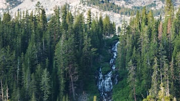 Una baita con veranda che si affaccia su un lago, circondata da fitta foresta e con le montagne sullo sfondo.