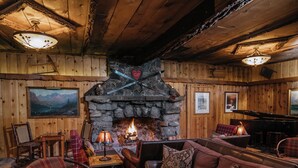 A cozy log cabin interior with a stone fireplace, wooden walls, and a piano. - Tamarack Lodge and Resort (Mammoth Lakes)