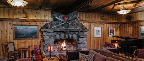 A cozy log cabin interior with a stone fireplace, wooden walls, and a piano.