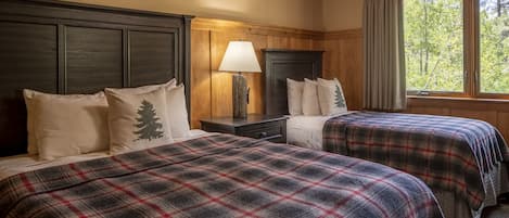 A room with two beds, wooden headboards, a nightstand with a lamp, and a window with curtains.