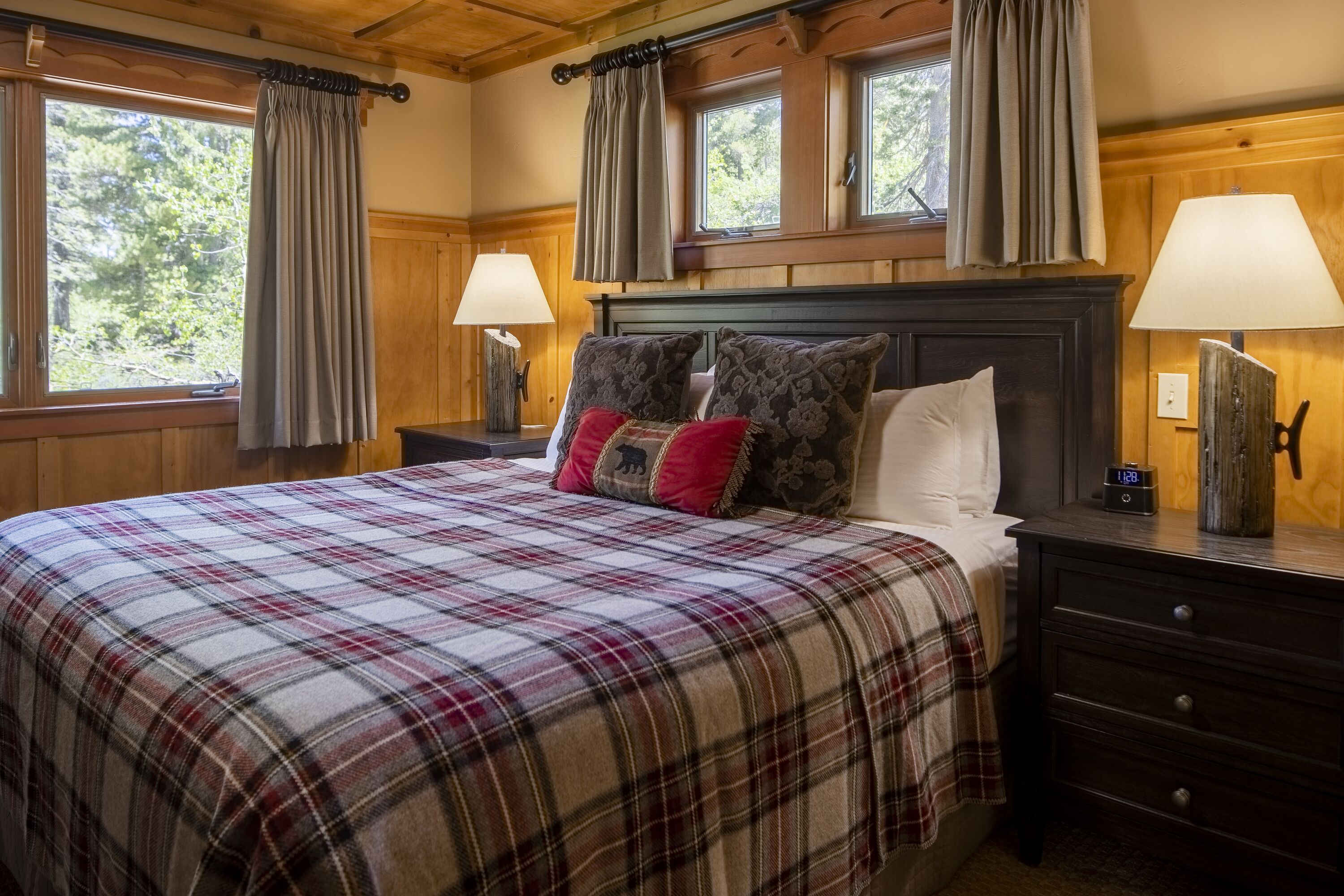 Une chambre à coucher avec une couvre-lit à carreaux, une tête de lit en bois, deux lampes de chevet et une table de chevet avec une horloge.