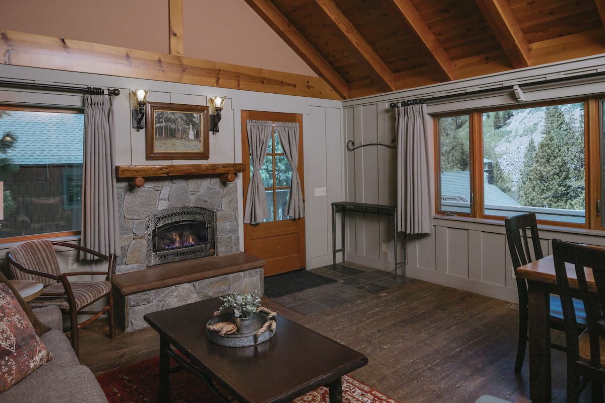 Ein gemütliches Wohnzimmer mit Kamin aus Stein, Holzbalken, einer Steinwand, einer hölzernen Bank, einer Couch und einem Esstisch.