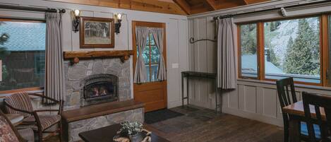 A cozy living room with a stone fireplace, wooden beams, a stone wall, a wooden bench, a sofa, and a dining table.