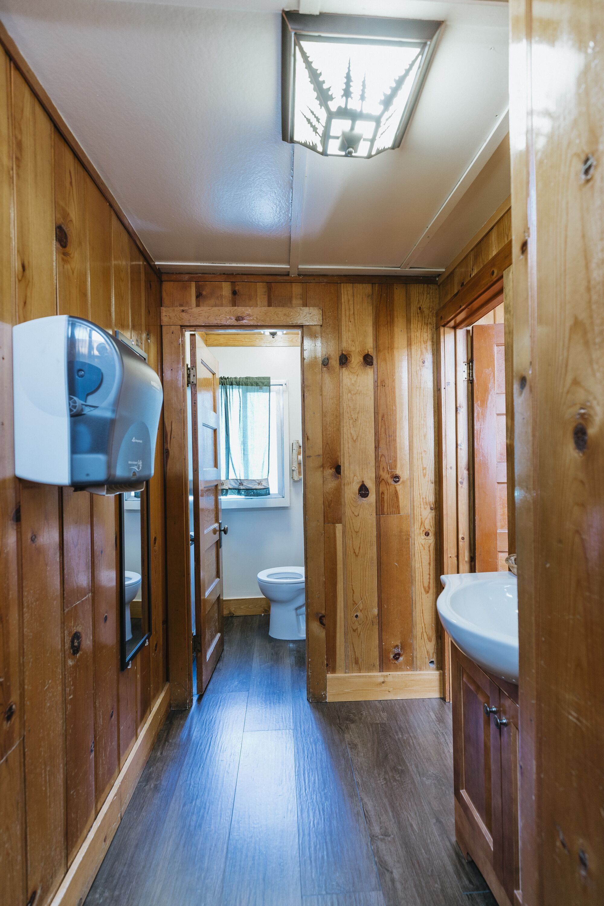 A narrow wooden hallway with a toilet, a sink, and a window with a view of trees.