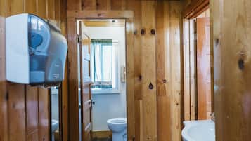 A narrow wooden hallway with a toilet, a sink, and a window with a view of trees.
