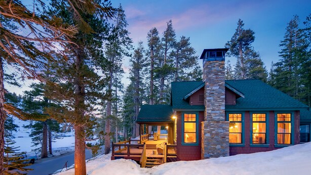A lodge with a stone chimney, wooden deck, and a view of the surrounding forest. - Tamarack Lodge and Resort (Mammoth Lakes)