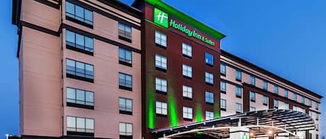 Edificio de Holiday Inn & Suites con diseño moderno, destacando una llamativa combinación de colores verde y rojo, varios pisos y un área de acceso cubierta.