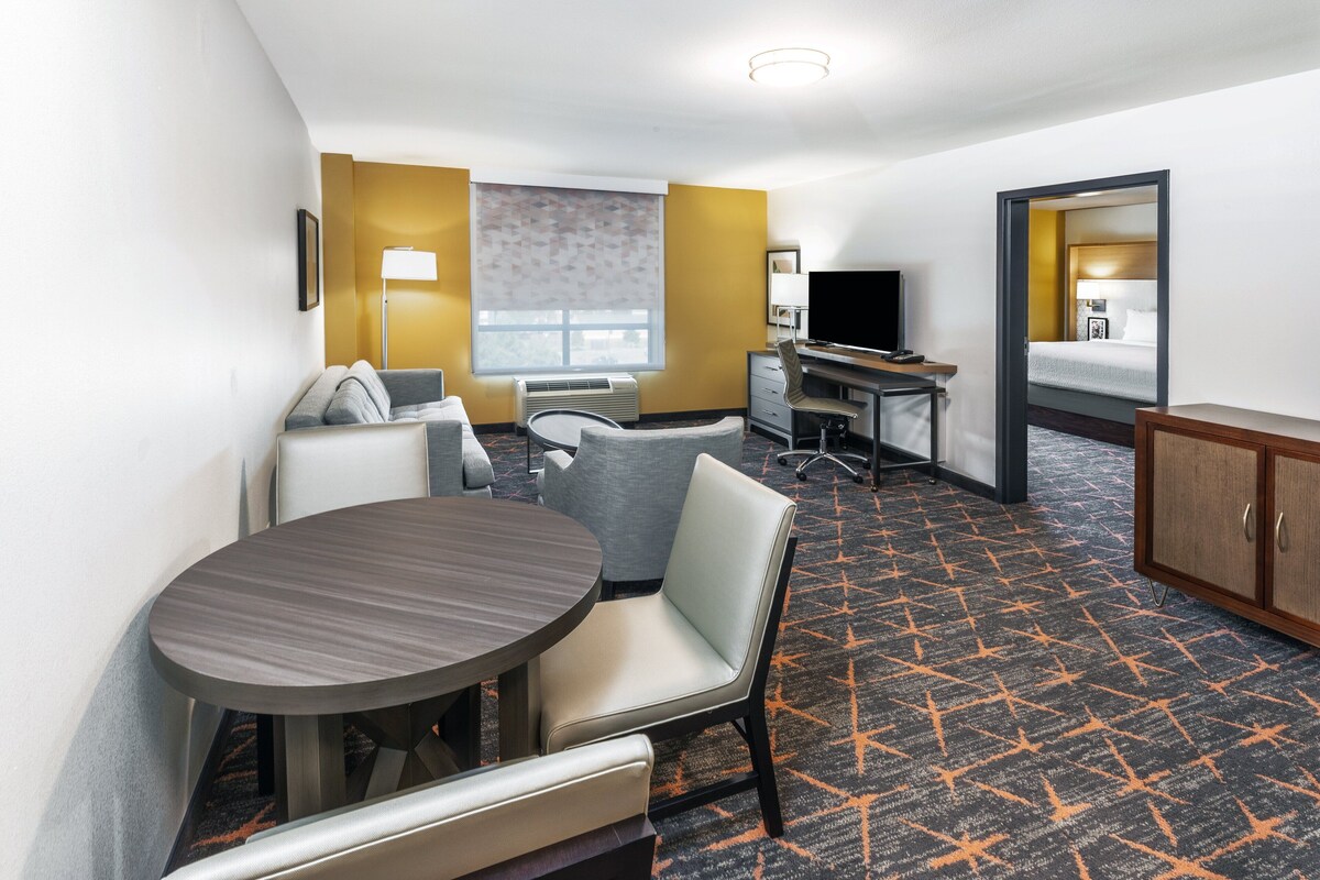 A hotel room with a bed, a desk, a chair, a TV, and a round table.