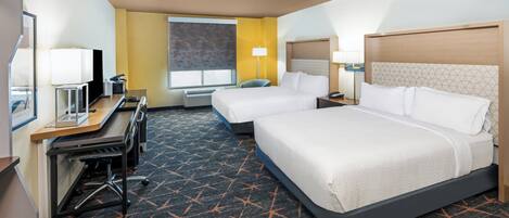 Habitación de hotel con dos camas, un escritorio, una silla, un ventanal con persianas y una alfombra de estampado geométrico.