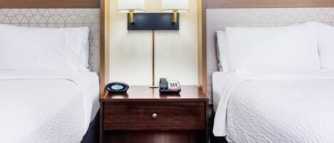A hotel room with two beds, a nightstand with a lamp, a phone, and a small table.