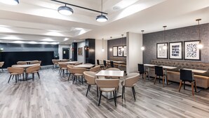 A modern restaurant with wooden flooring, round tables, and beige chairs. - Holiday Inn Hotel & Suites Tulsa South by IHG (Tulsa)