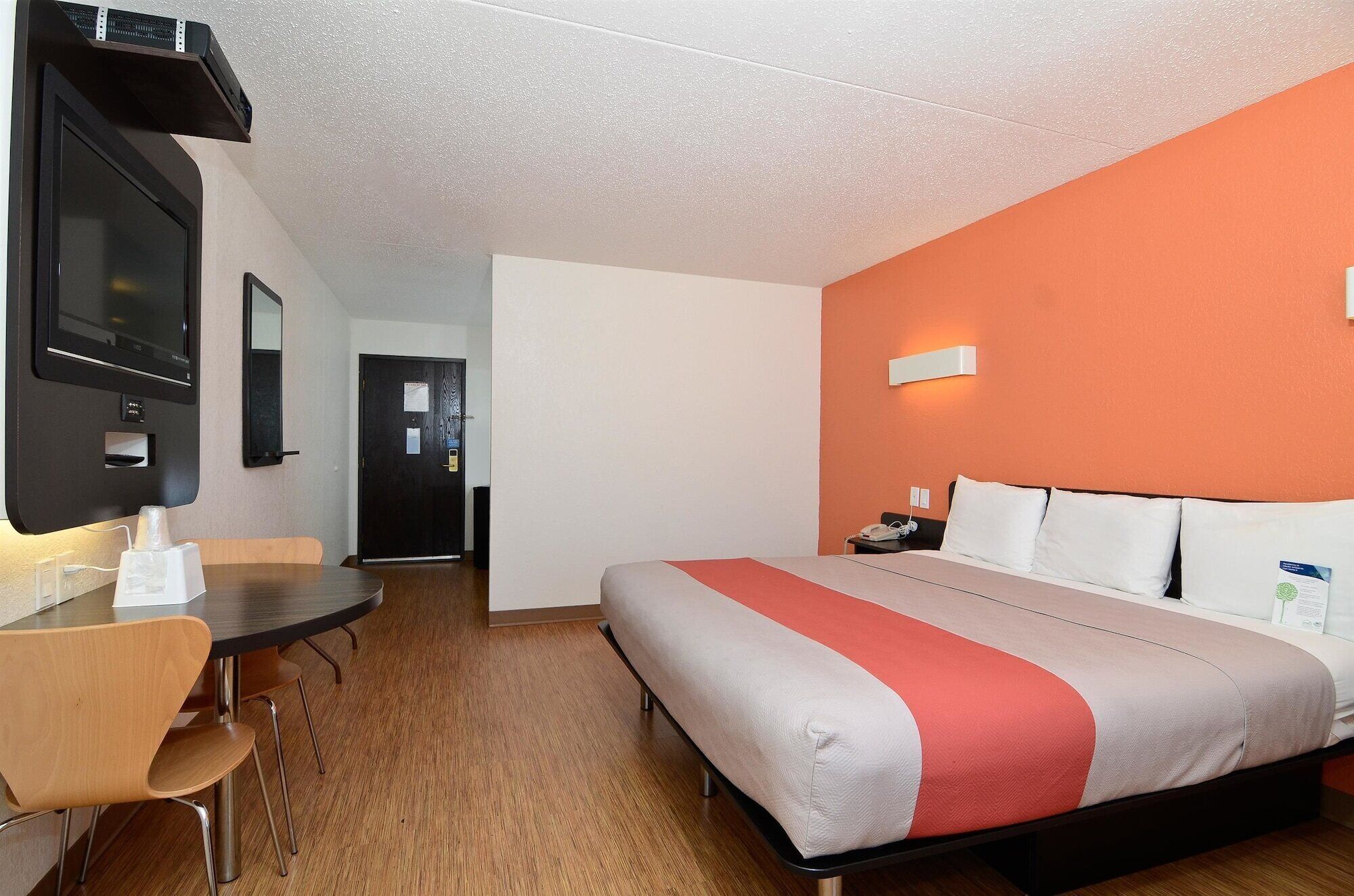 A hotel room with a bed, a desk, a chair, a TV, and a door.