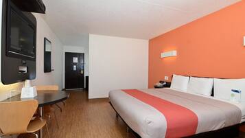 A hotel room with a bed, a desk, a chair, a TV, and a door.