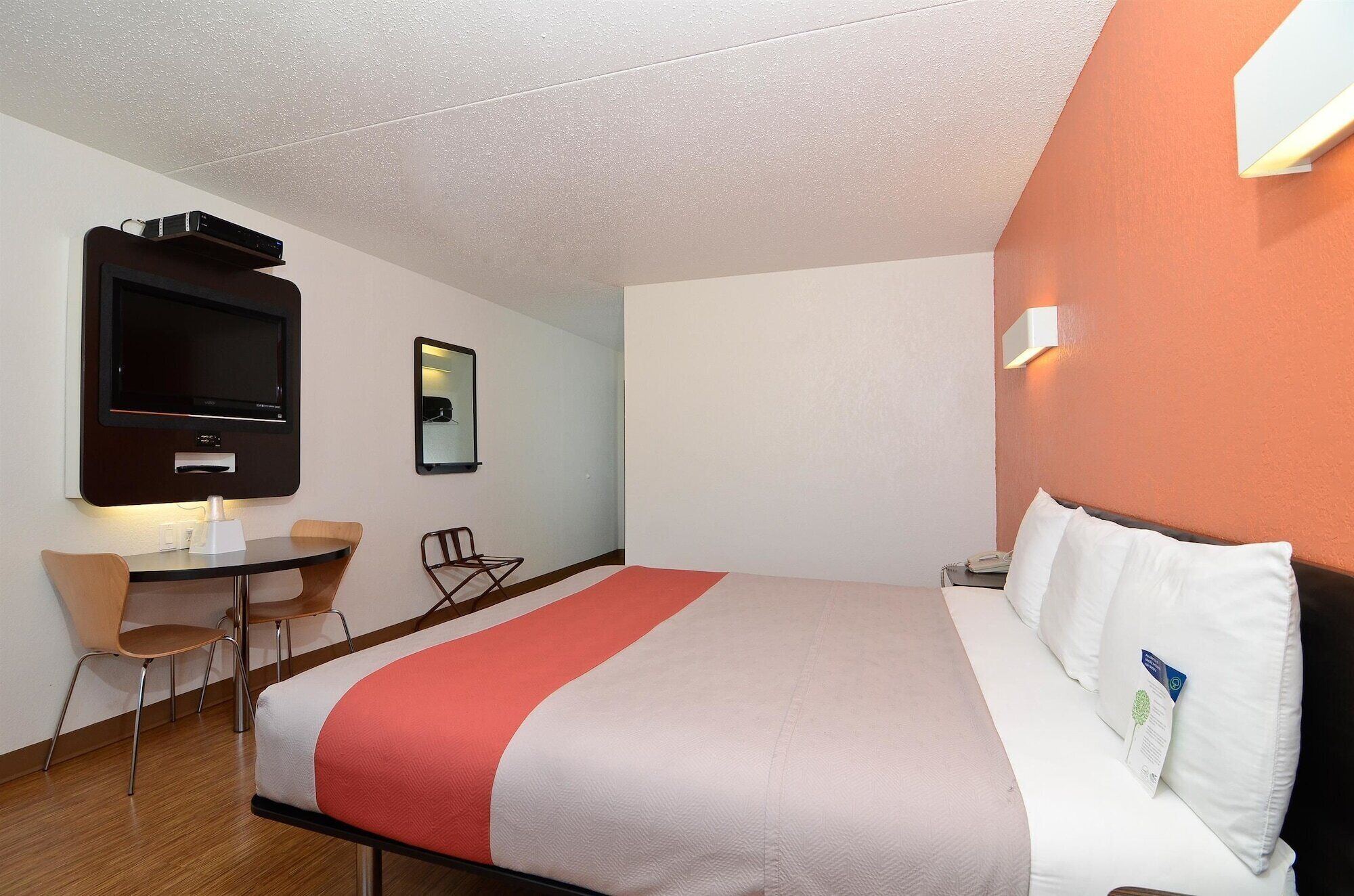 A hotel room with a bed, a desk with a chair, a television, and a mirror.