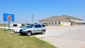 Un motel avec une grande enseigne indiquant qu’il s’agit du numéro 6, un parking avec plusieurs voitures et un bâtiment doté d’un toit plat et d’une seule étage.