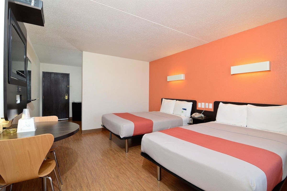 Habitación de hotel con dos camas, un escritorio, una silla y un televisor.