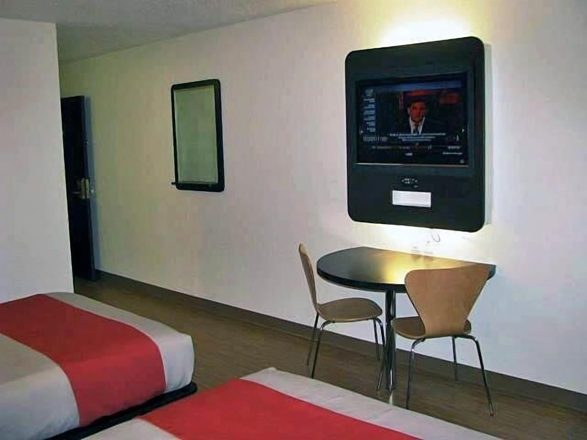Une chambre d’hôtel avec deux lits, un téléviseur fixé au mur et une petite table avec deux chaises.