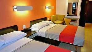 Une chambre d’hôtel avec deux lits, un petit bureau, une chaise et un miroir.