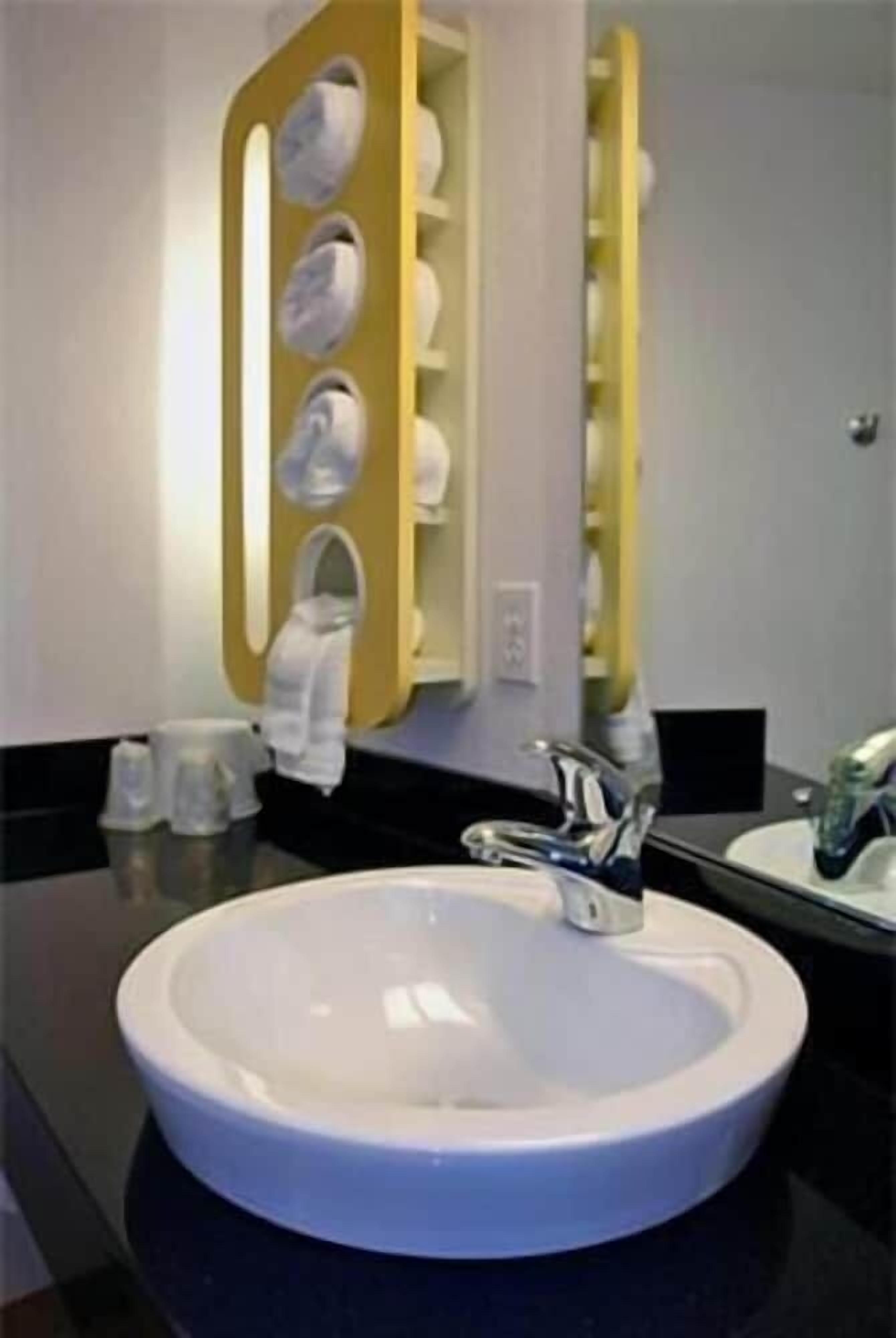 A bathroom with a round white sink, a mirror, and a towel rack.