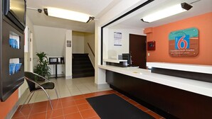 Un espace d’accueil comprenant un comptoir, un bureau, un ordinateur, une enseigne indiquant un motel à six chambres et un escalier.