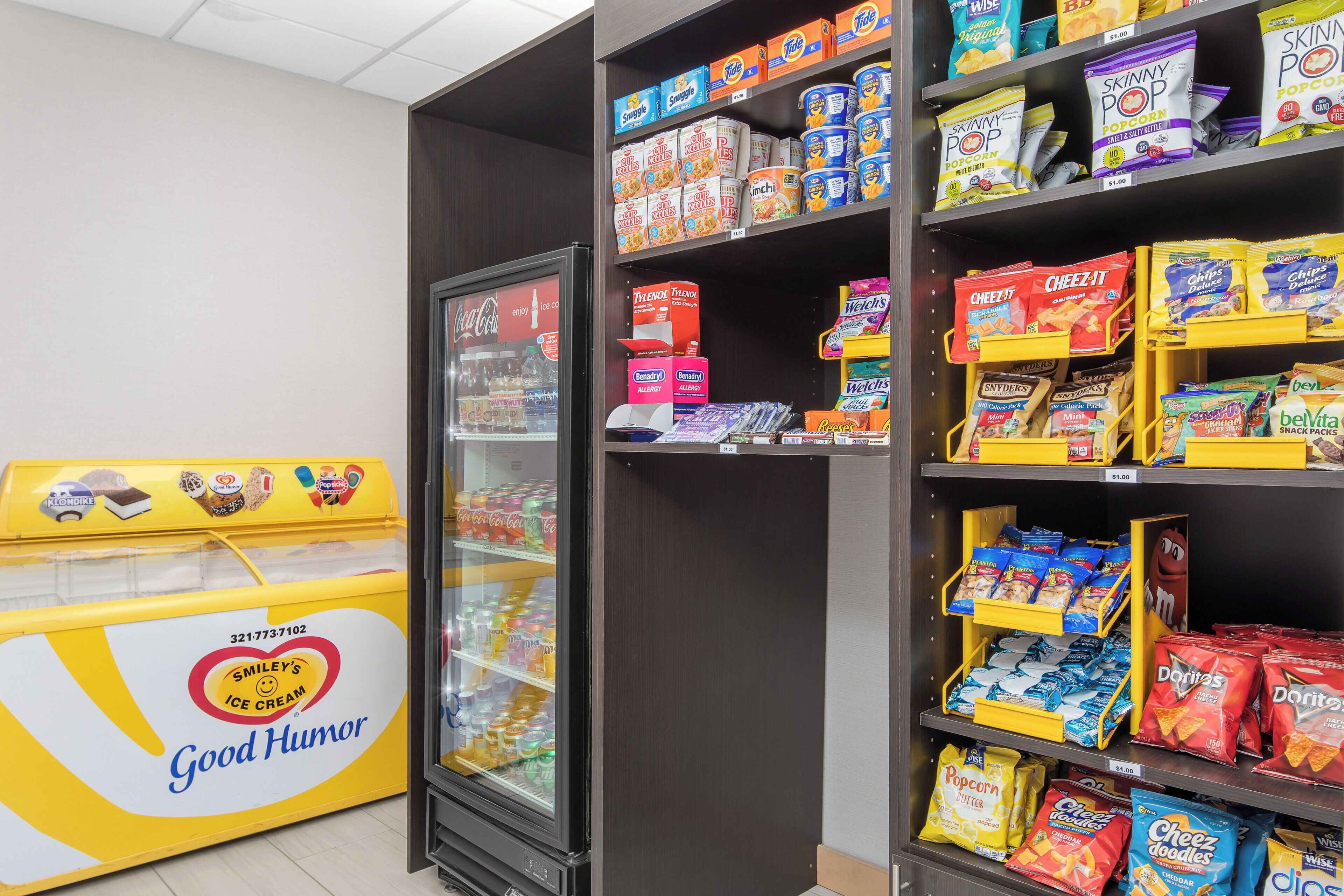 A snack aisle in a store with various packaged snacks and a refrigerator with ice cream.