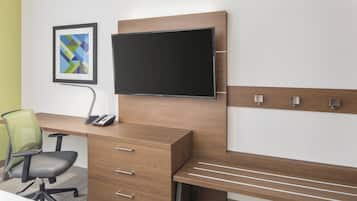 Habitación de hotel con escritorio de madera, televisor de pantalla plana, teléfono, silla de malla verde y una cómoda.