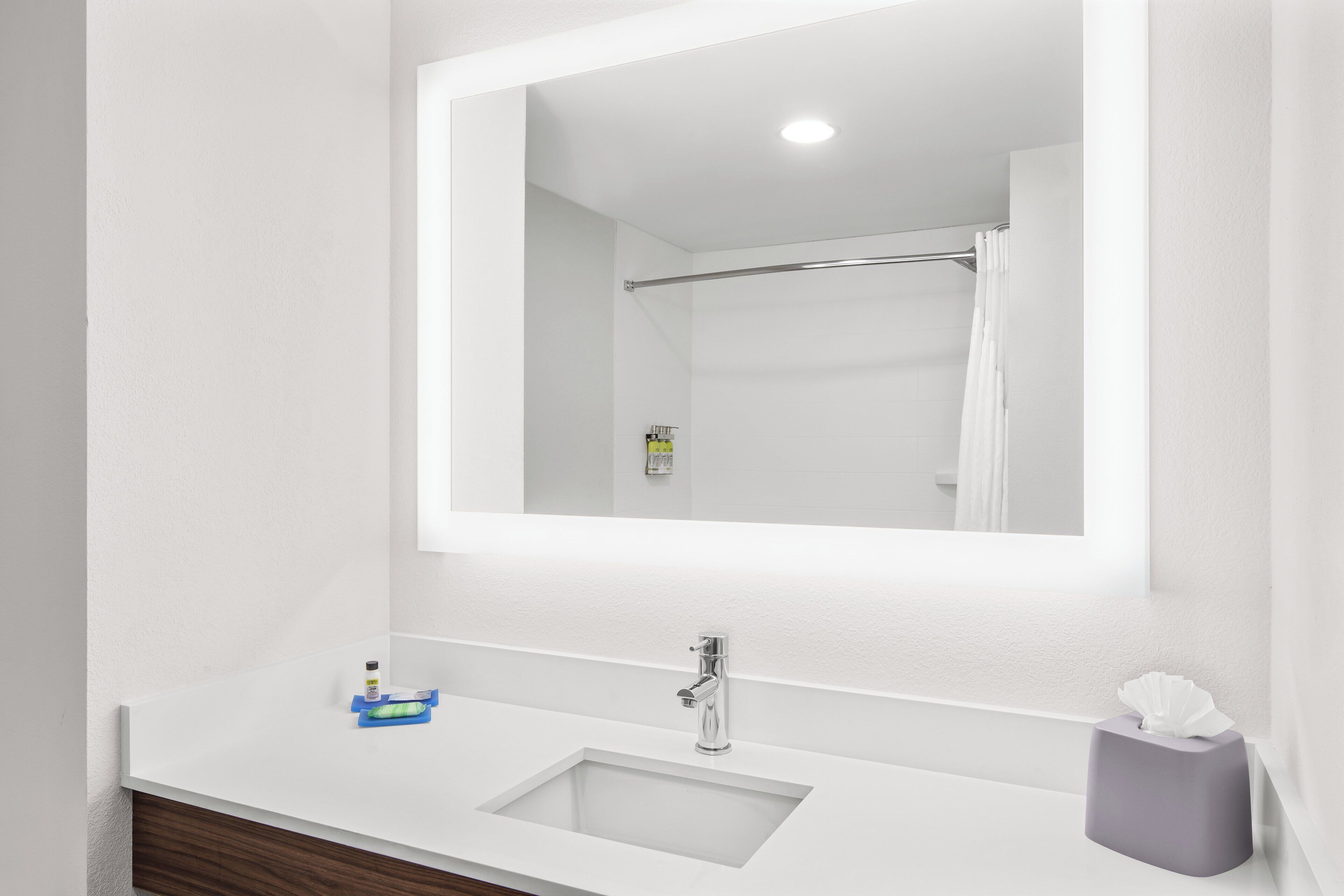 A bathroom with a white sink, a mirror, a towel dispenser, and a shower curtain.