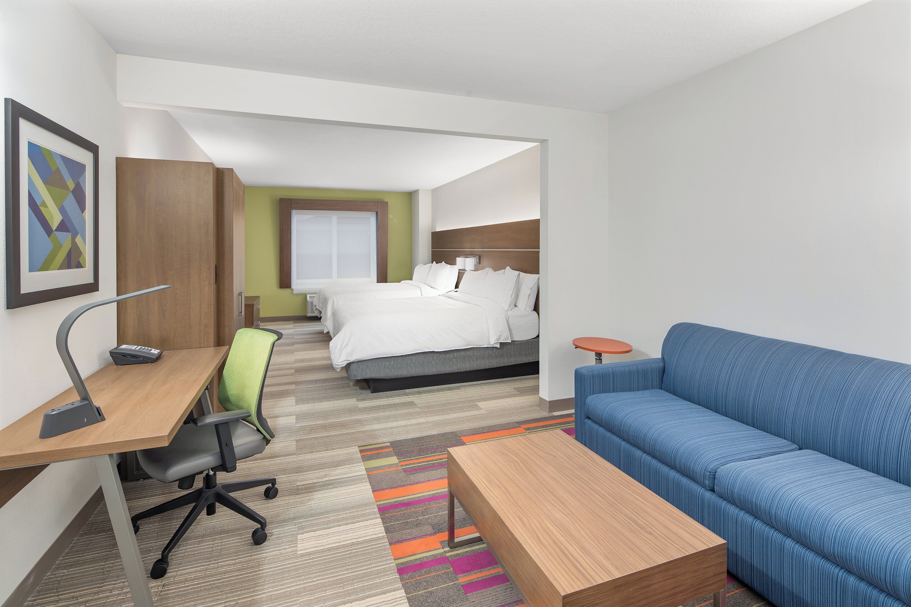 A hotel room with a desk, office chair, bed, blue sofa, and a small round table.