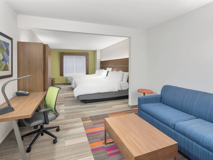 A hotel room with a desk, office chair, bed, blue sofa, and a small round table.