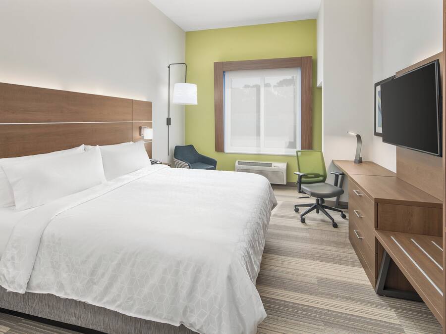 Una habitación de hotel con cama, escritorio, silla, televisor y ventana.