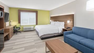 Een hotelkamer met een bed, een blauwe bank, een houten bureau, een stoel, een televisie en een raam.