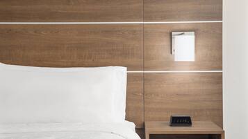 A neatly made bed with white linens, a wooden headboard, and a bedside table with a digital clock.