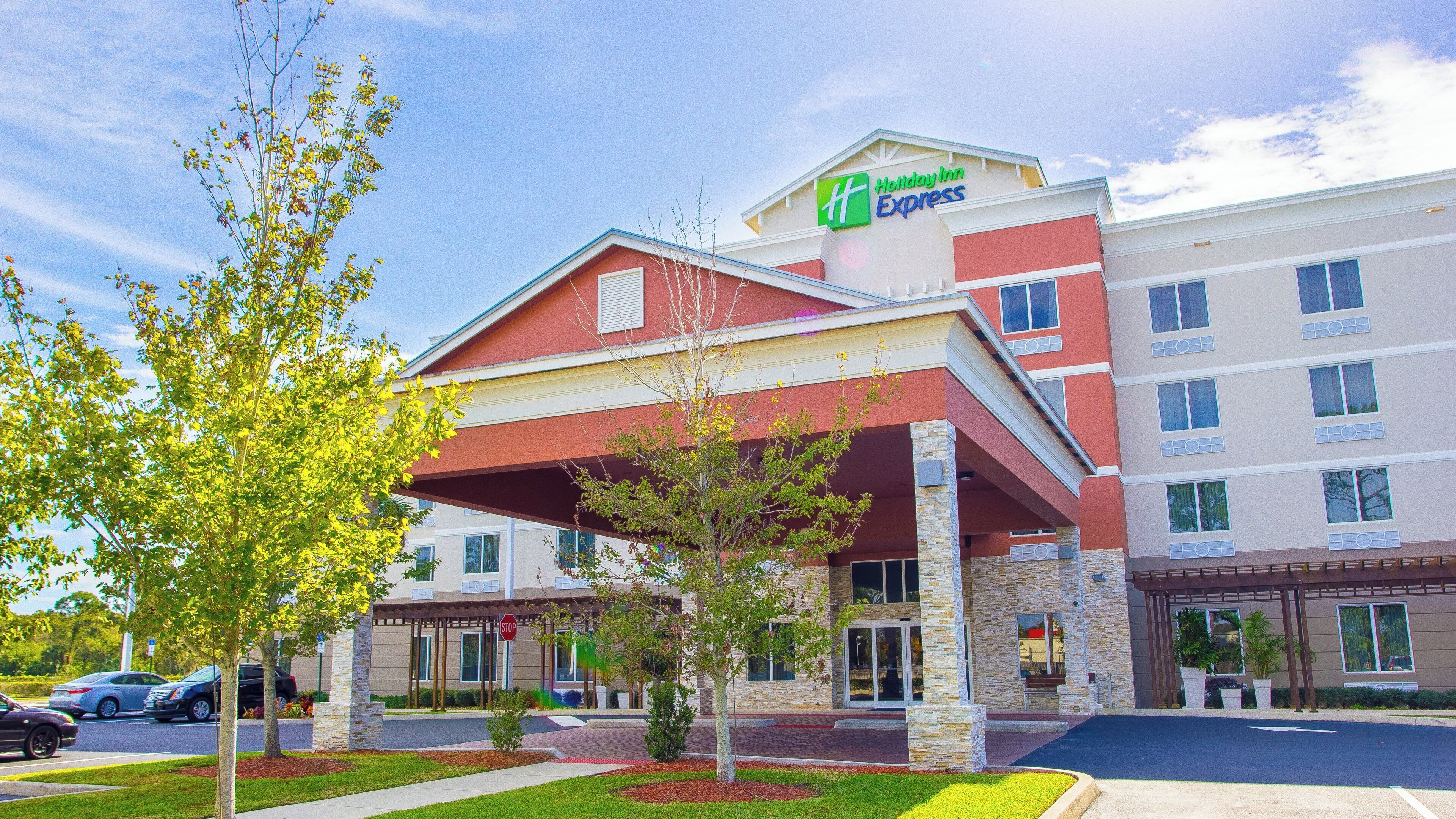 Ein Holiday Inn Express Hotel mit rotem und beigem Fassadendekor, einer überdachten Eingangspforte und einem Parkplatz.