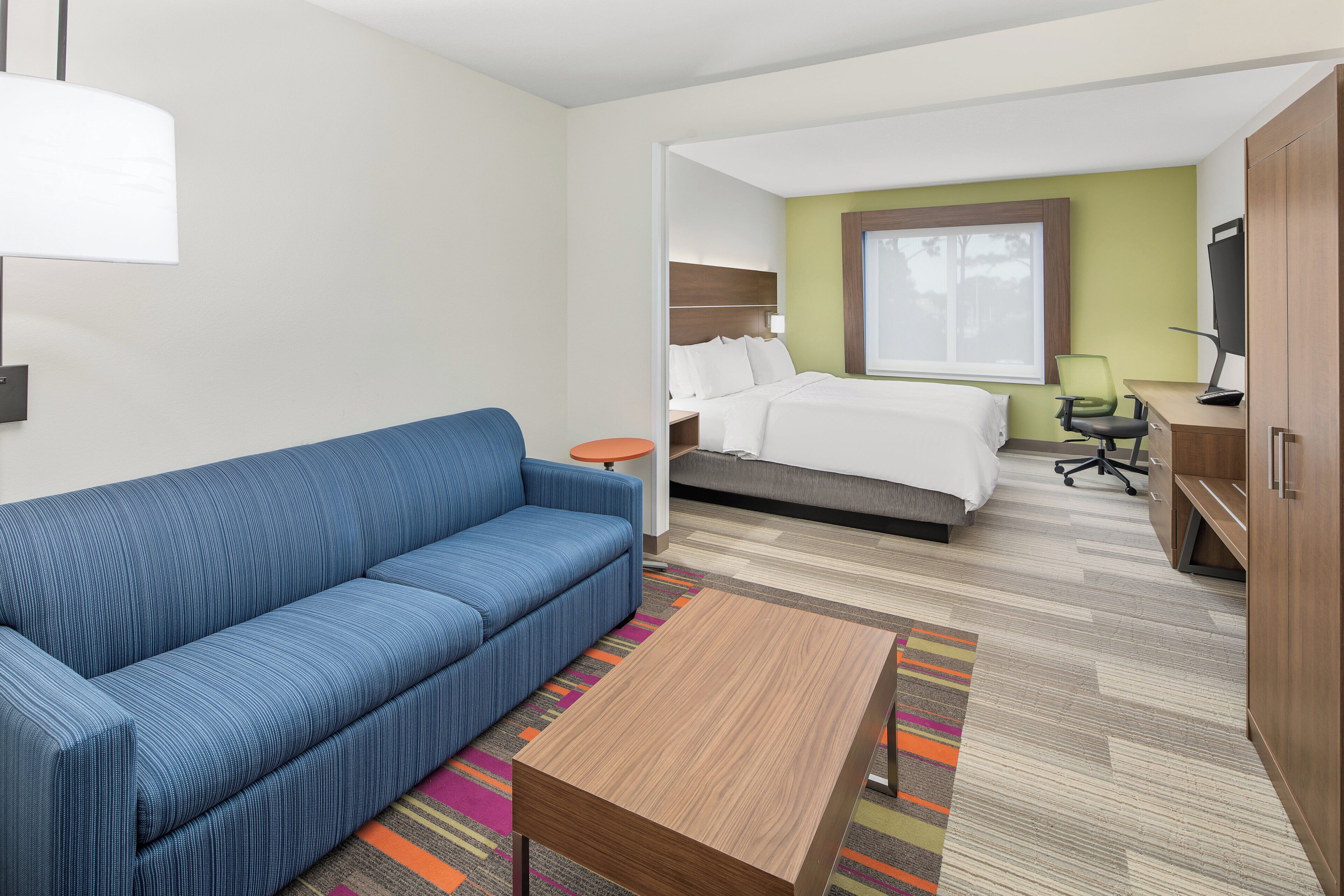A hotel room with a blue sofa, a bed, a desk with a chair, and a TV.
