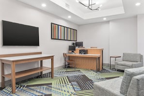 Ein modernes Hotelzimmer mit einem Flachbildfernseher, einem Schreibtisch mit Computer, Drucker und einem bequemen Sessel.