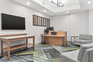 A modern hotel room with a flat-screen TV, a desk with a computer, a printer, and a comfortable armchair.
